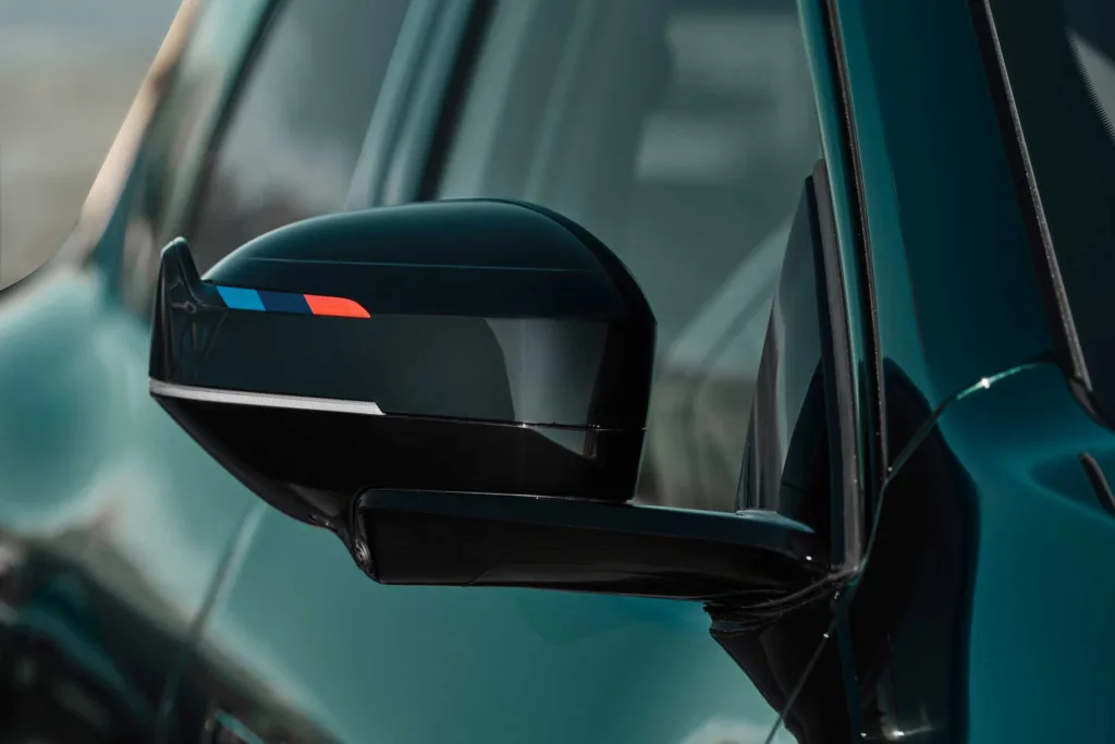 Espejo retrovisor del BMW iX3 M60 xDrive con franjas de color M sobre fondo negro