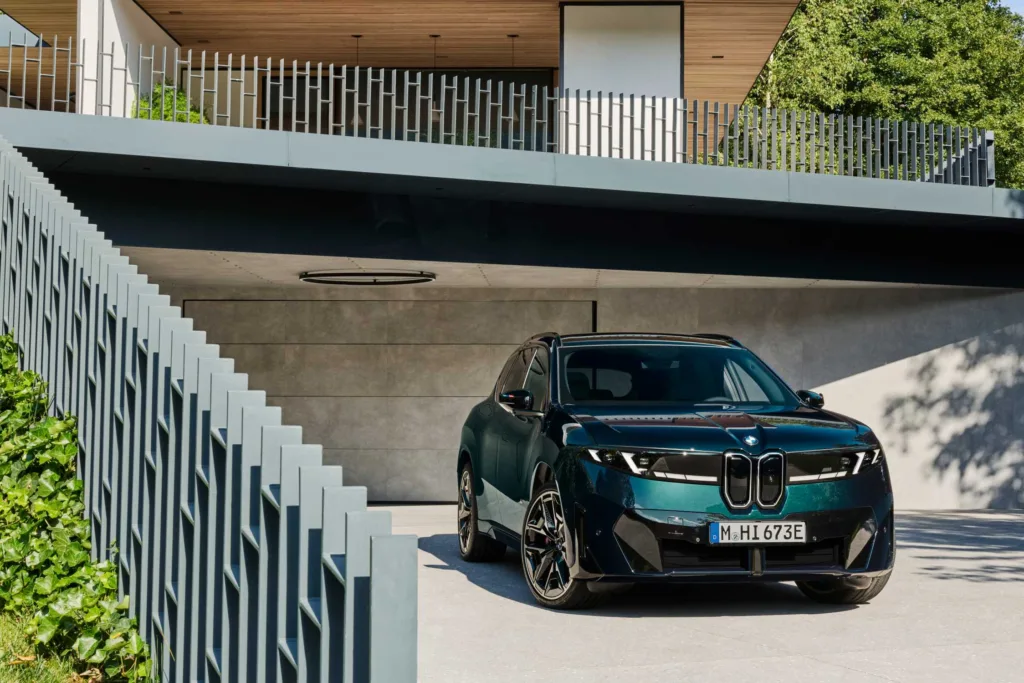 BMW iX3 M60 xDrive estacionado bajo una estructura moderna de concreto y madera, vista frontal tres cuartos
