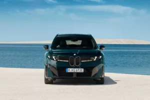 Frente del BMW iX3 M60 xDrive estacionado frente al mar con cielo azul
