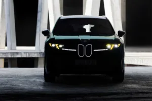 Frente del BMW iX3 M60 xDrive con las luces amarillas encendidas entre pilares de concreto