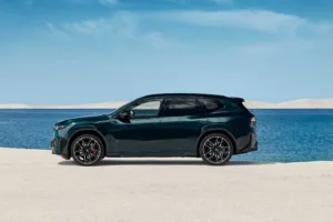 Perfil del BMW iX3 M60 xDrive frente al mar, con llantas negras