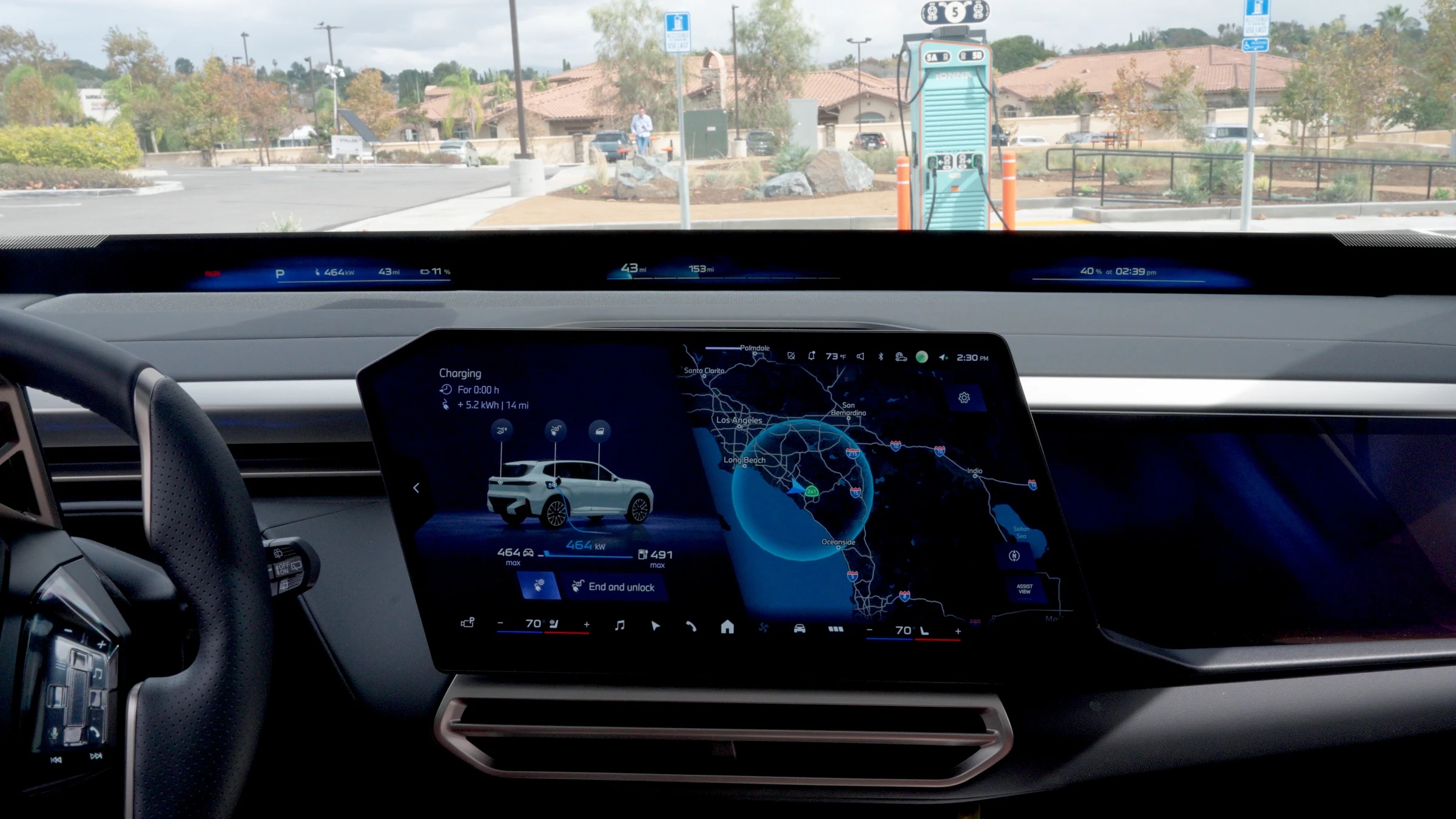Pantalla central del BMW iX5 con un mapa de la zona, vista desde el asiento del conductor, con un cargador al fondo