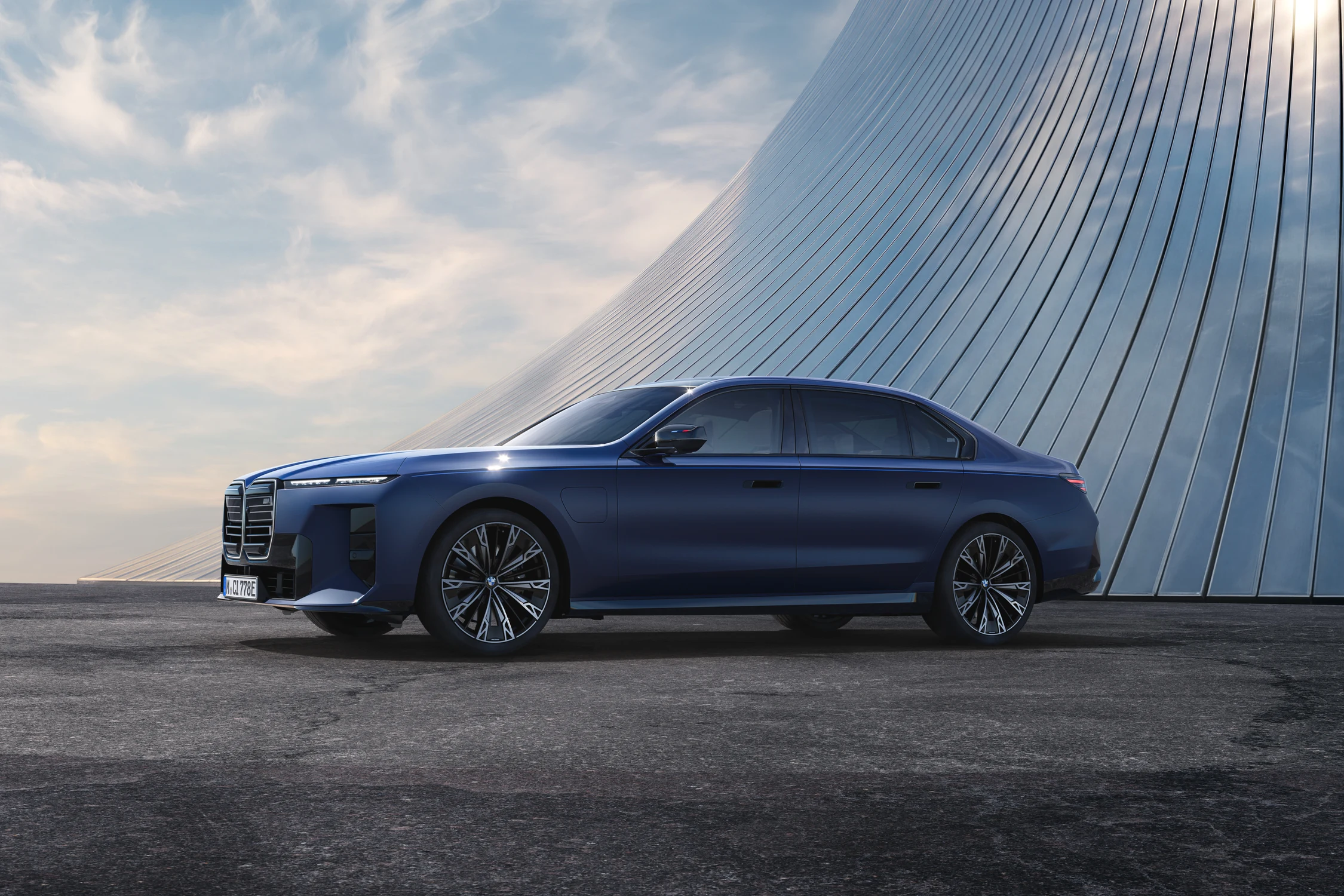 BMW Serie 7 M760e xDrive azul visto de costado frente a una estructura curva de metal, con llantas de 22 pulgadas