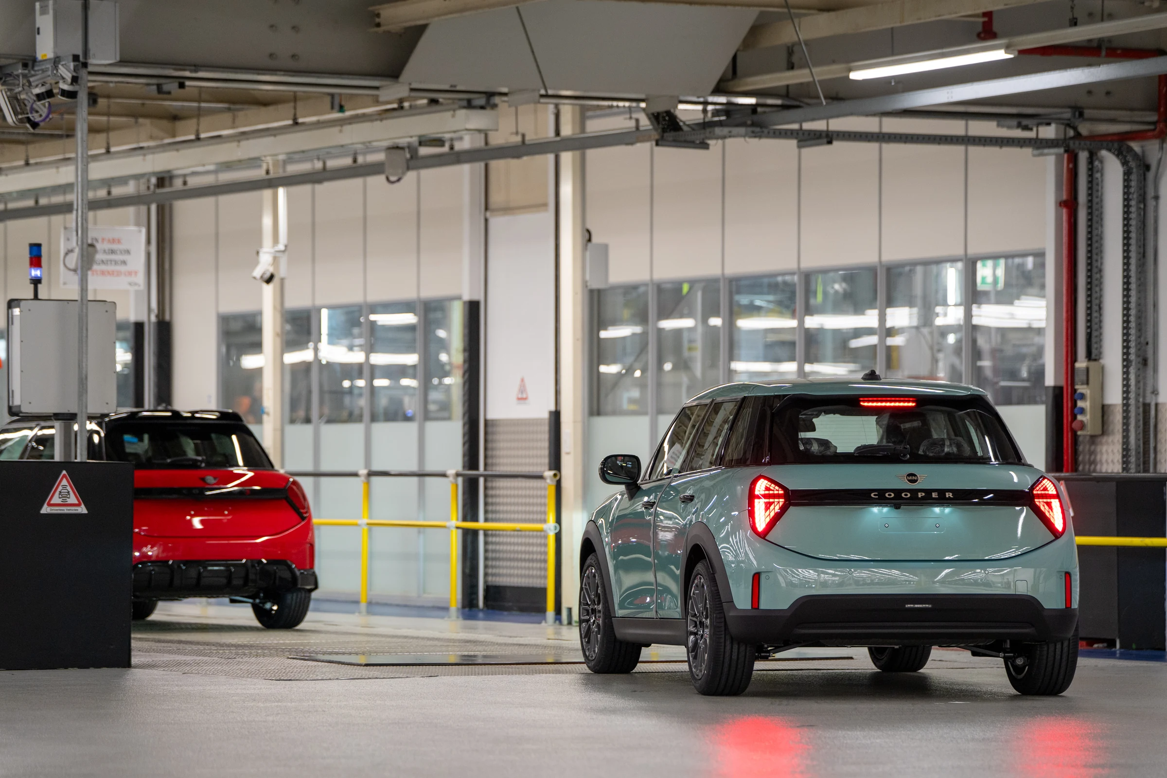 MINI Cooper verde agua visto desde atrás en la planta de Oxford, con un auto rojo al fondo