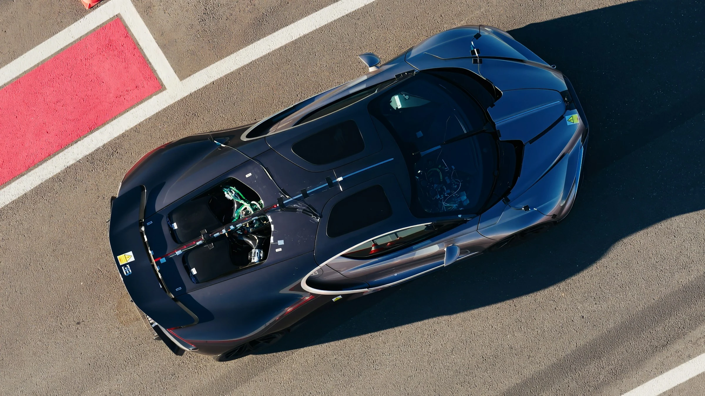 Vista desde arriba de un prototipo del Bugatti Tourbillon azul oscuro con el capó abierto sobre el asfalto