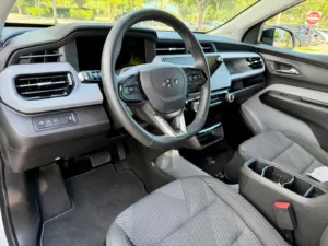 Puesto de conducción del Chevrolet Bolt 2027 visto desde la puerta del conductor, con volante y asientos de tela