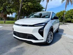 Chevrolet Bolt 2027 blanco, vista frontal tres cuartos, estacionado junto a unas palmeras