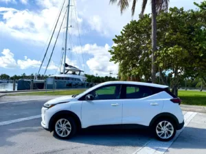Perfil del Chevrolet Bolt 2027 blanco con llantas de aleación, frente a un embarcadero