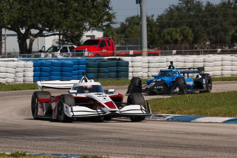 Dallara IR28 de la IndyCar en pista junto a otro monoplaza azul en Sebring
