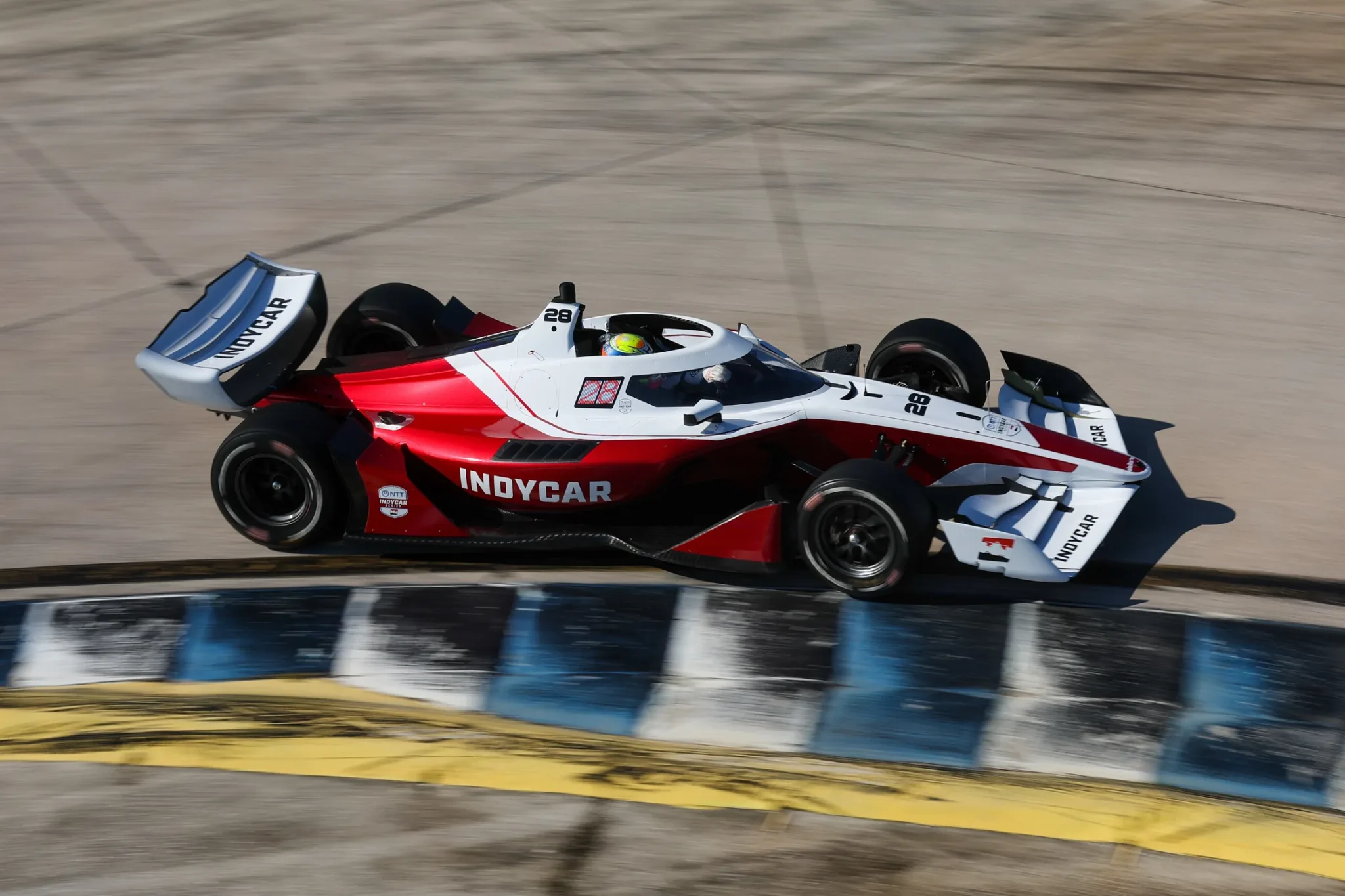 Dallara IR28 rojo y blanco en pista sobre el piano de una curva de Sebring