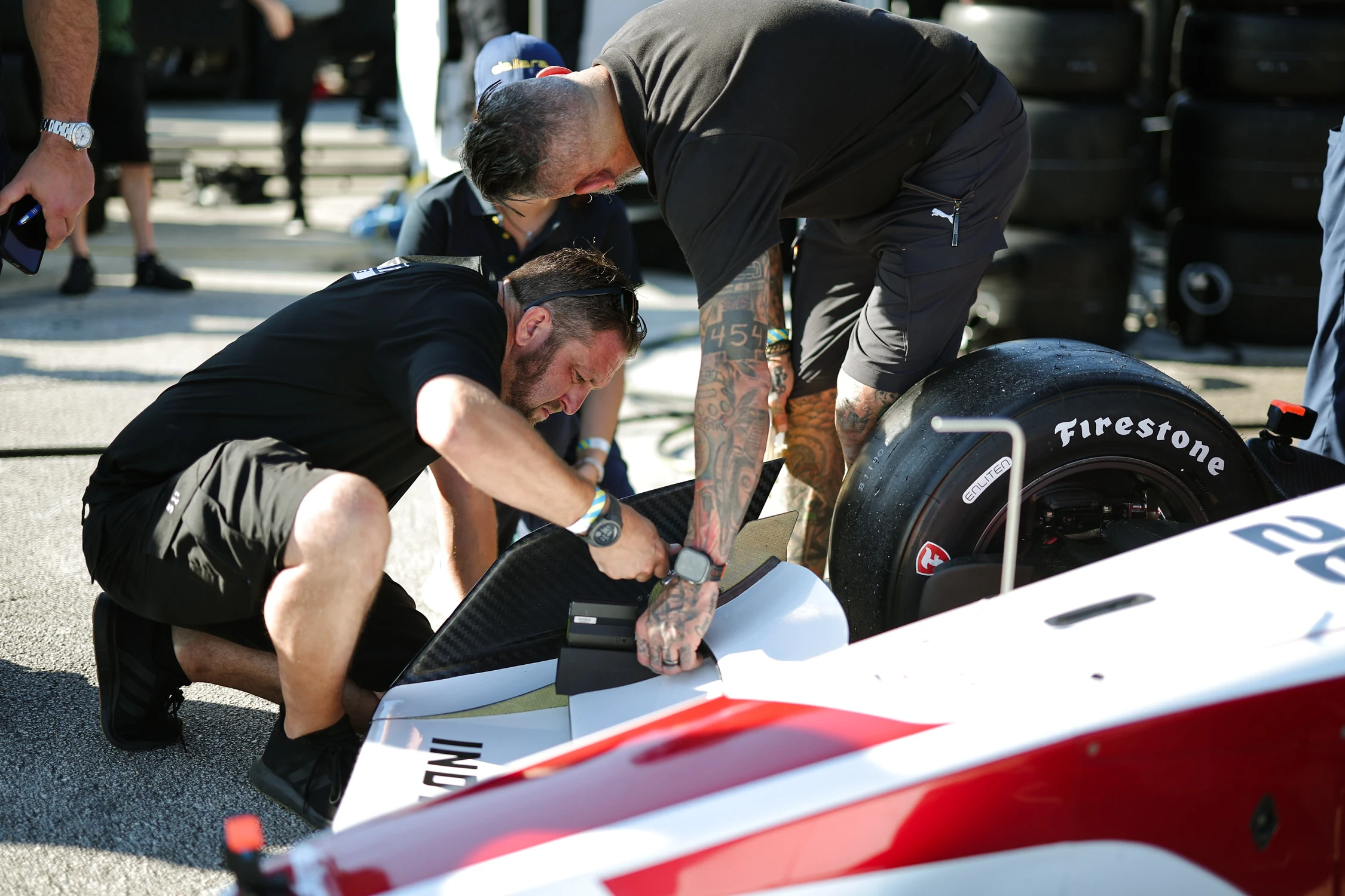Mecánicos ajustando la parte delantera del Dallara IR28 junto a un neumático Firestone