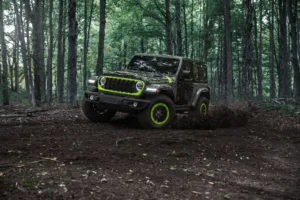 Jeep Wrangler Switchback 2027 de frente, con la parrilla de acentos Gecko y las llantas verdes, en un camino de bosque