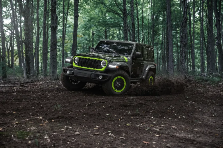 Jeep Wrangler Switchback 2027 de frente, con la parrilla de acentos Gecko y las llantas verdes, en un camino de bosque