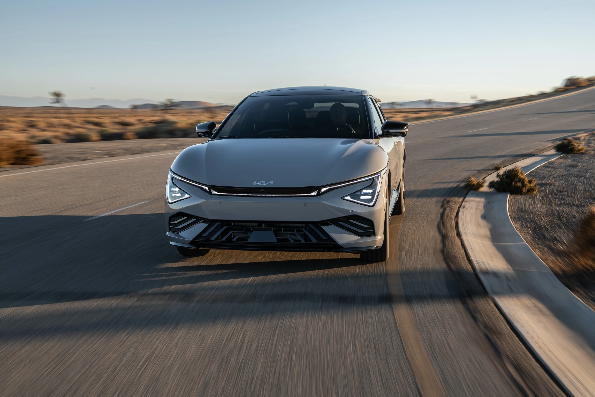 Frente del Kia EV6 gris, con la barra de luces diurnas y la toma de aire inferior, en una curva del desierto