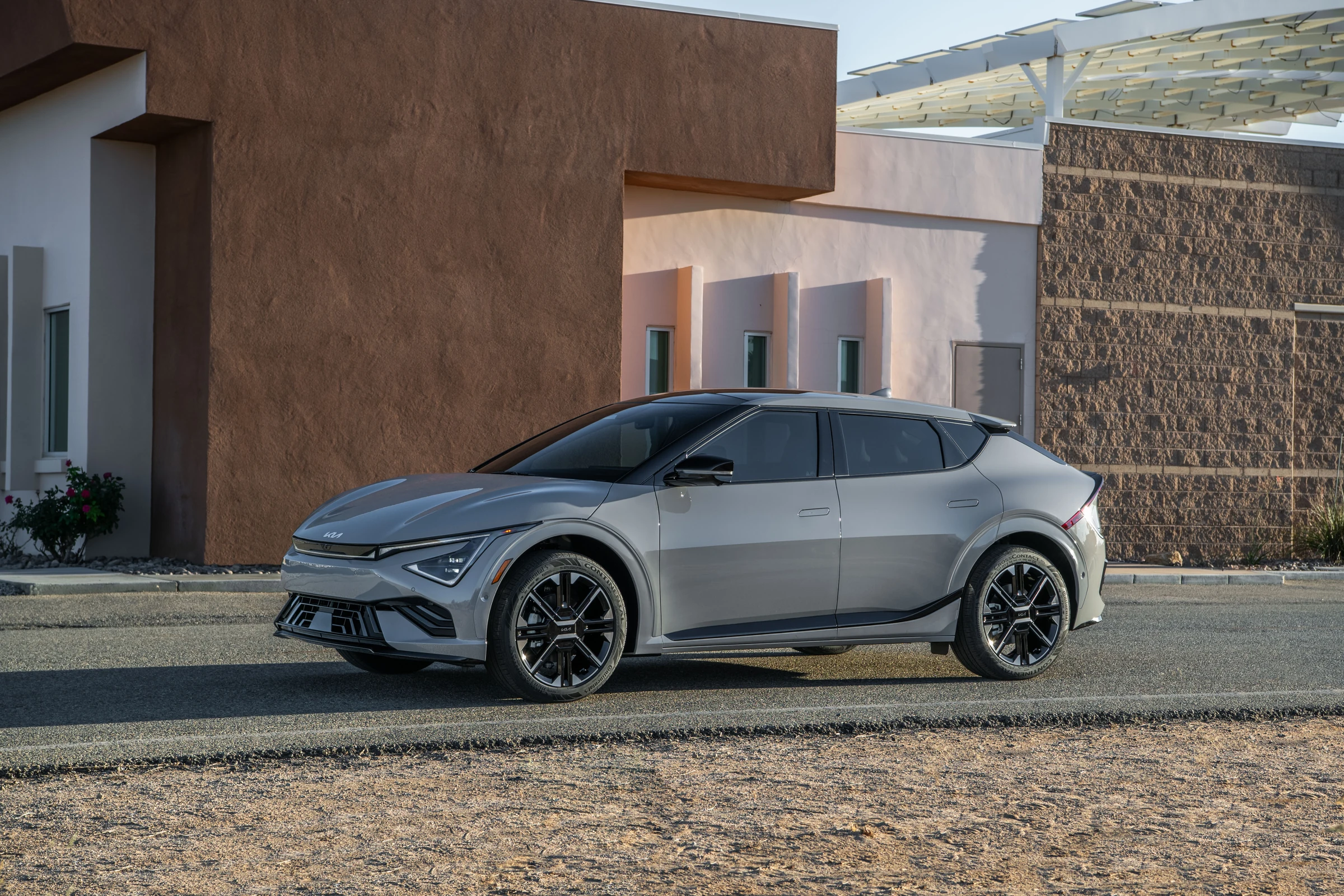 Kia EV6 gris de tres cuartos frontales, estacionado frente a un edificio rosado y marrón con paneles solares
