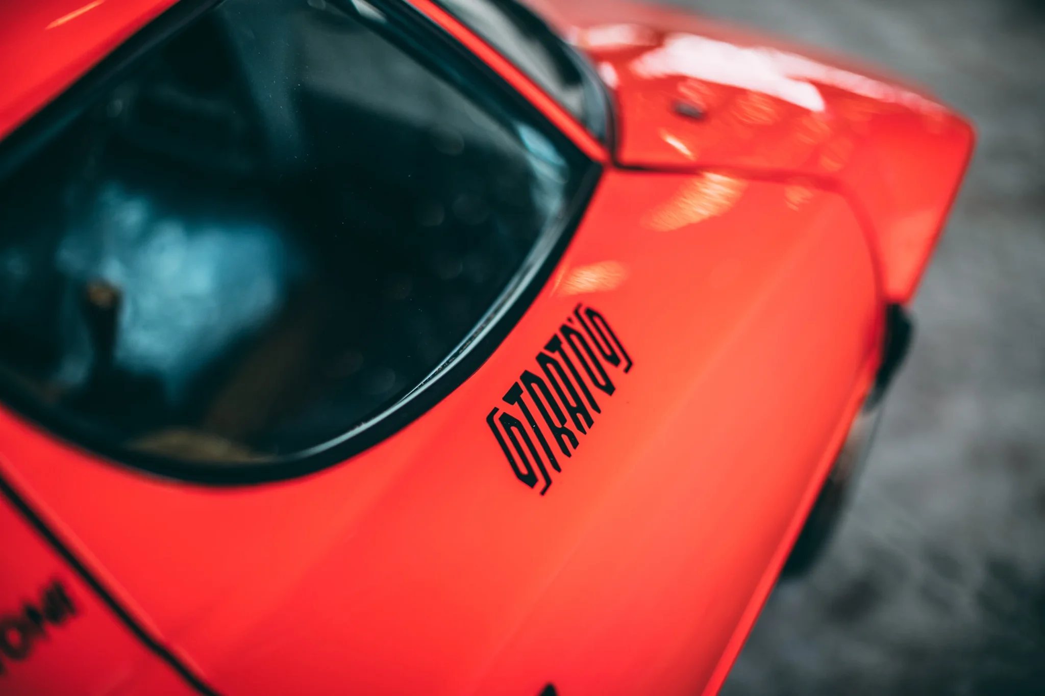 Detalle lateral de un Lancia Stratos naranja, con el nombre Stratos en la carrocería