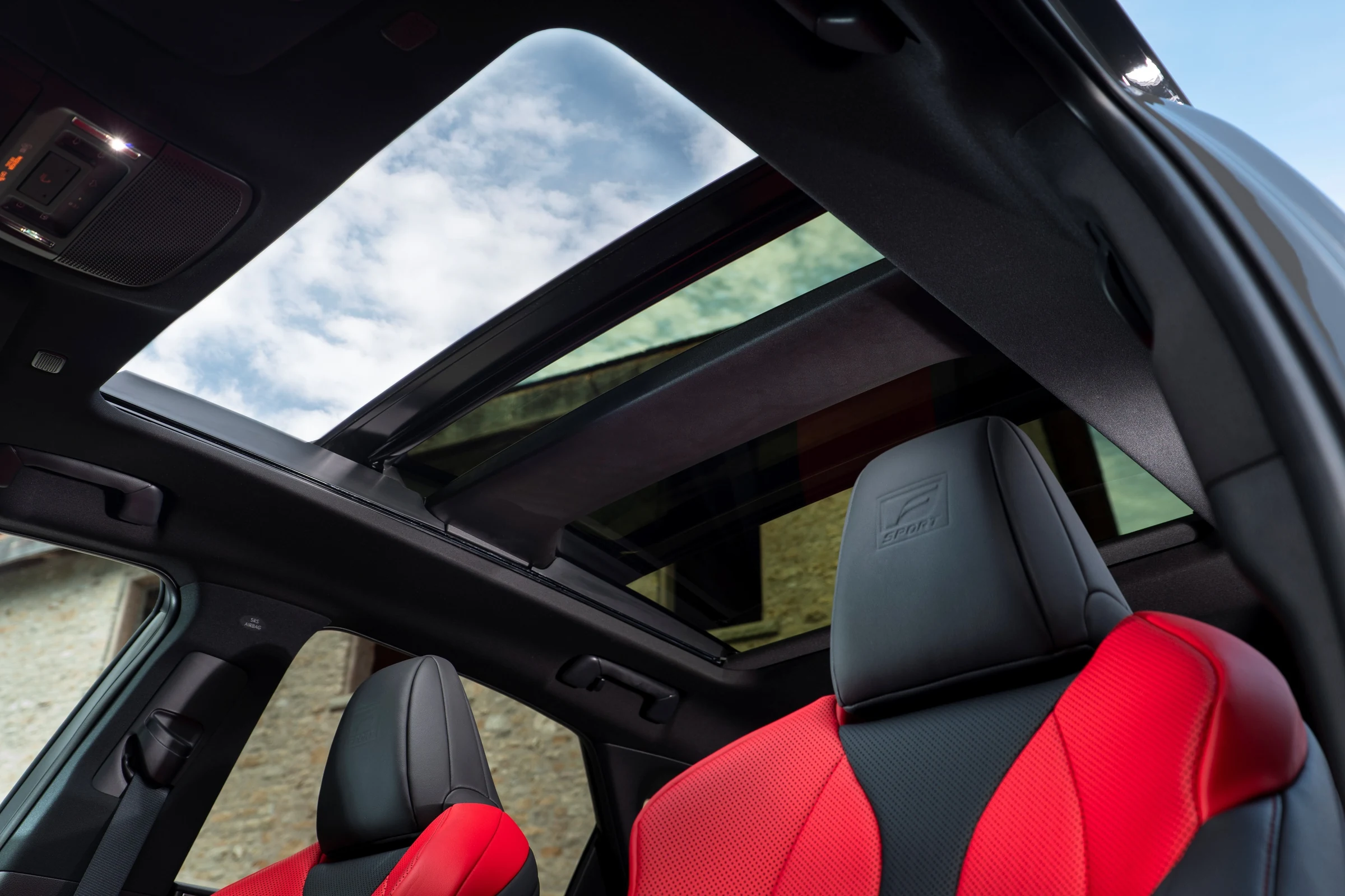 Interior del Lexus NX 2027 F SPORT con asientos negros y rojos y el techo solar panorámico sobre un cielo nublado
