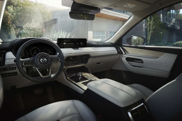 Tablero y consola del Mazda CX-90 vistos desde el asiento trasero, con cuero claro y pantalla central