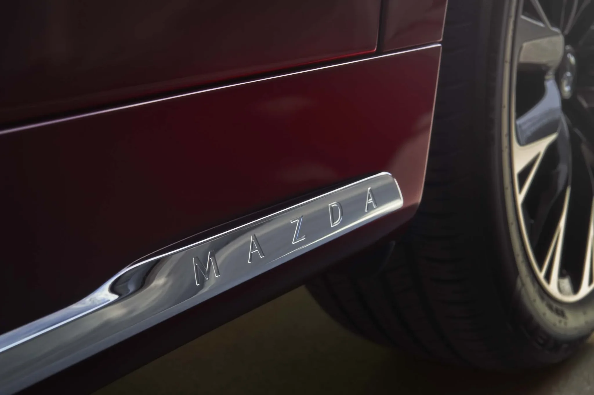 Moldura cromada con la palabra Mazda en el umbral de un CX-90 rojo, junto a la rueda
