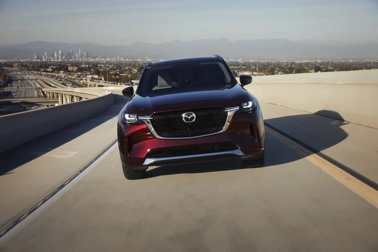 Mazda CX-90 rojo visto de frente, en marcha por una autopista elevada al atardecer