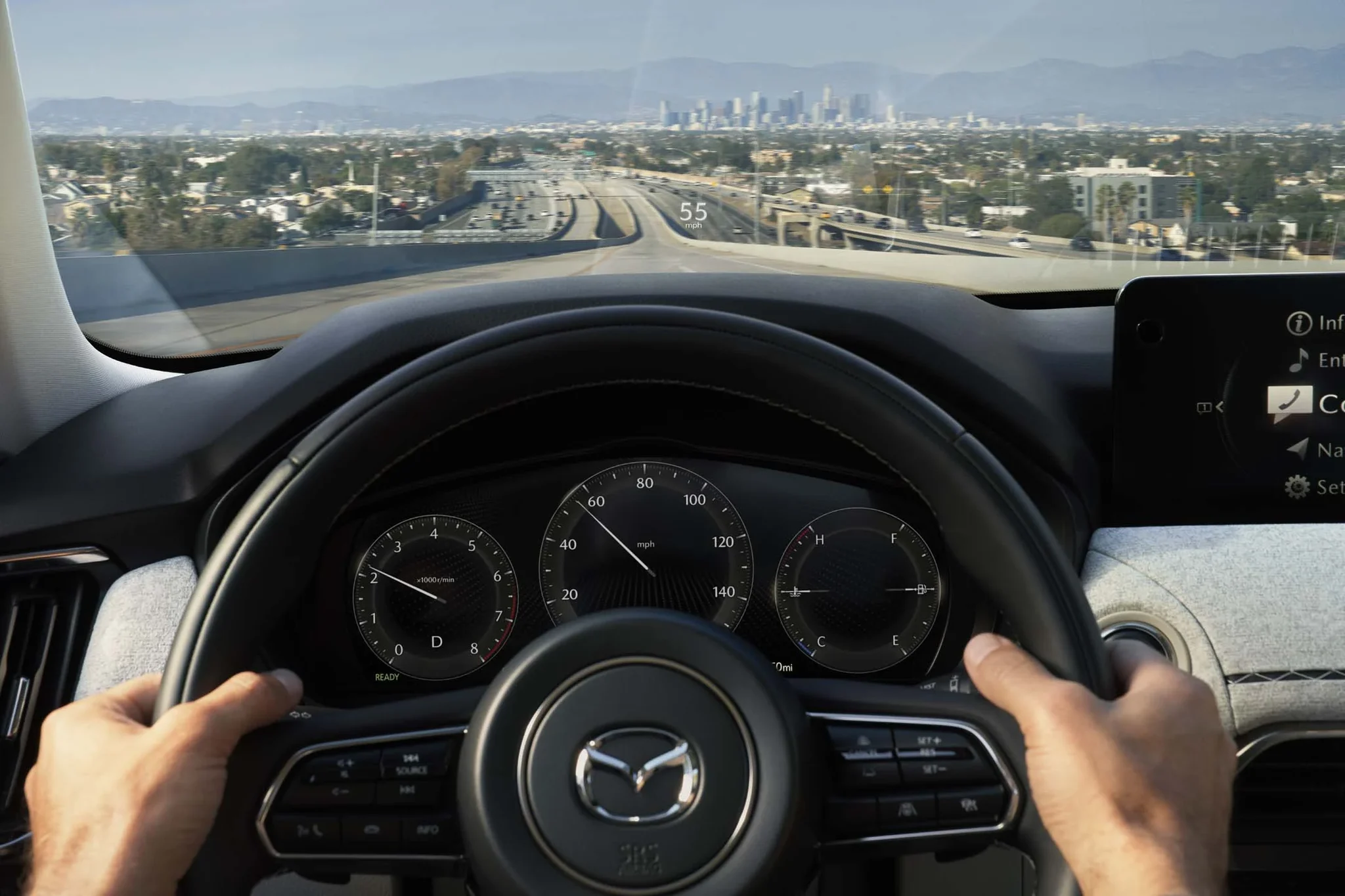 Manos sobre el volante del Mazda CX-90, con el tablero de instrumentos y una autopista de fondo