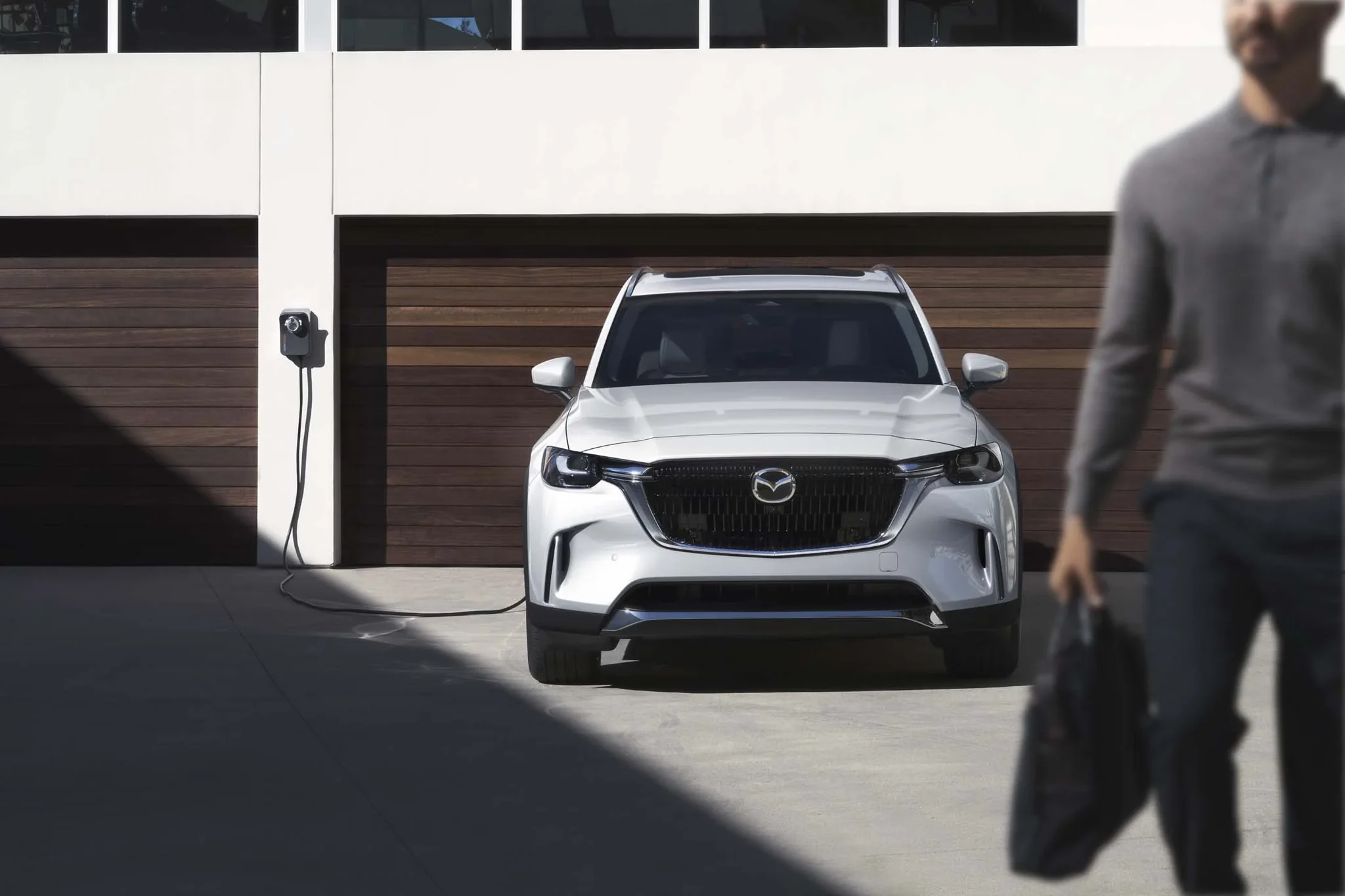 Mazda CX-90 híbrido enchufable blanco, de frente, conectado a un cargador en la entrada de un garaje