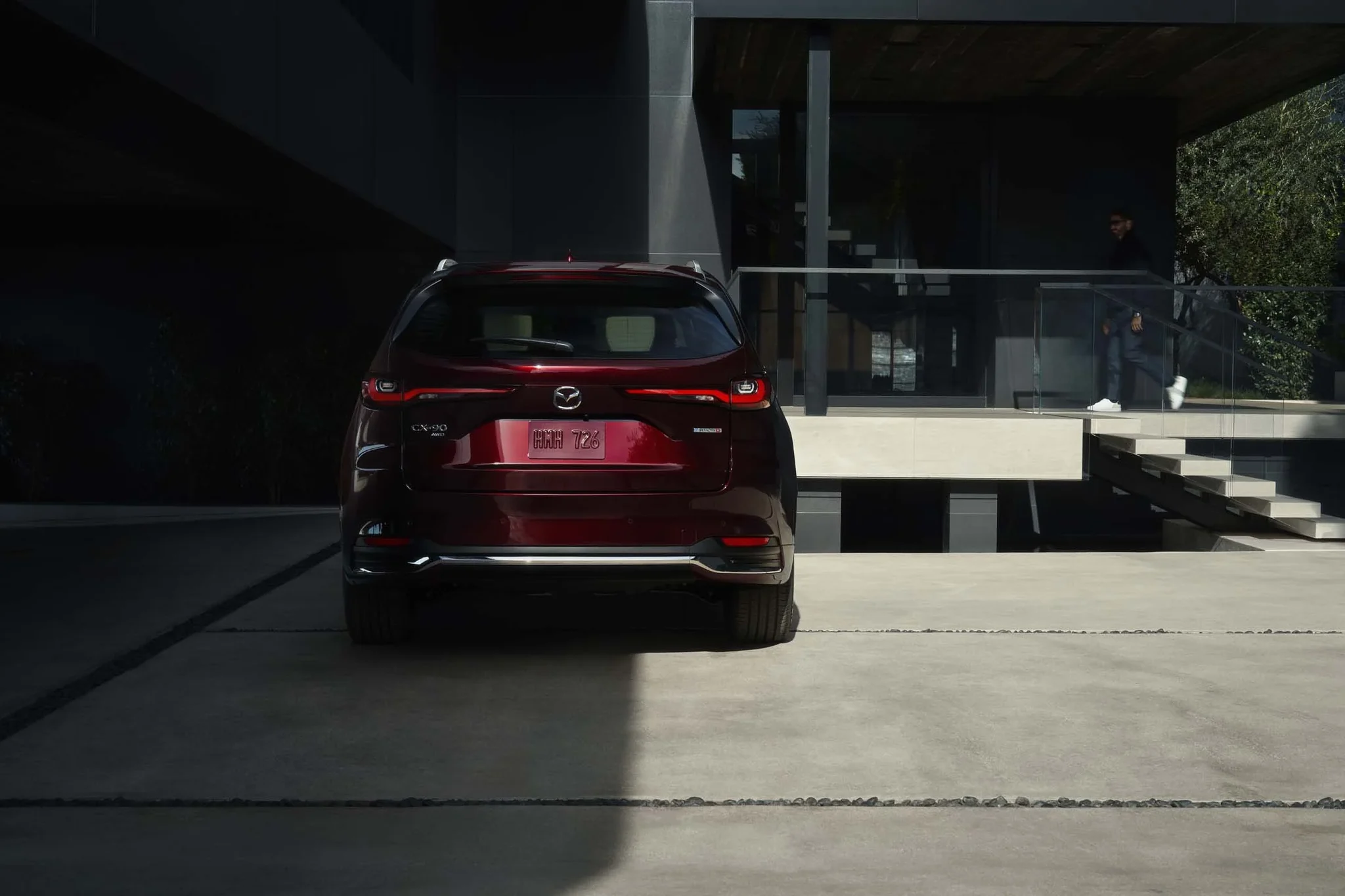 Mazda CX-90 rojo visto desde atrás, estacionado frente a un edificio moderno de vidrio y concreto