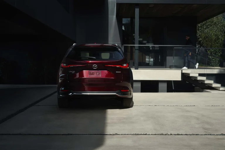 Mazda CX-90 rojo visto desde atrás, estacionado frente a un edificio moderno de vidrio y concreto