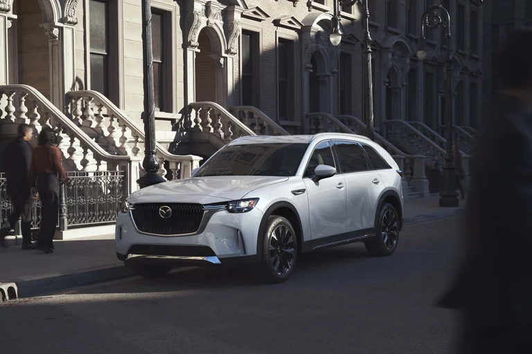 Mazda CX-90 blanco de tres cuartos frontales junto a una acera con escalinatas de piedra