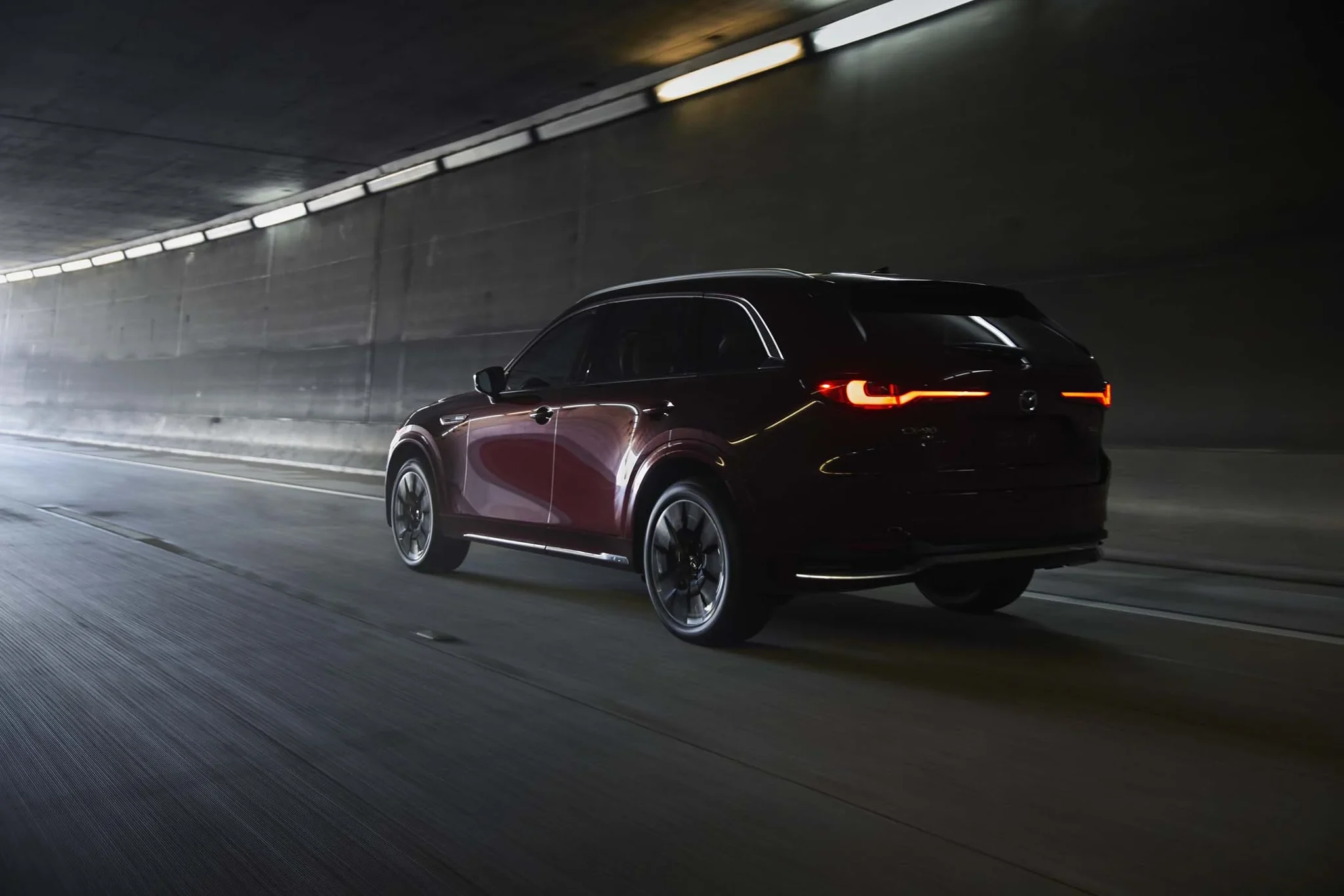 Mazda CX-90 rojo oscuro de tres cuartos traseros dentro de un túnel, con las luces traseras encendidas