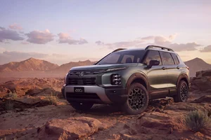 Mitsubishi Outlander Diamond Trail Edition 2028 en verde, de tres cuartos frontales, sobre un terreno rocoso al atardecer