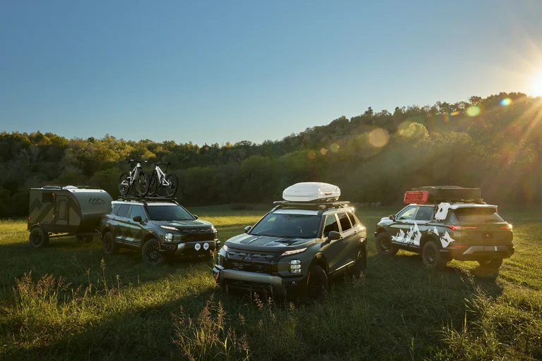 Los tres Outlander Diamond Trail que Mitsubishi mostrará en el SEMA, junto a un remolque, en un prado al atardecer