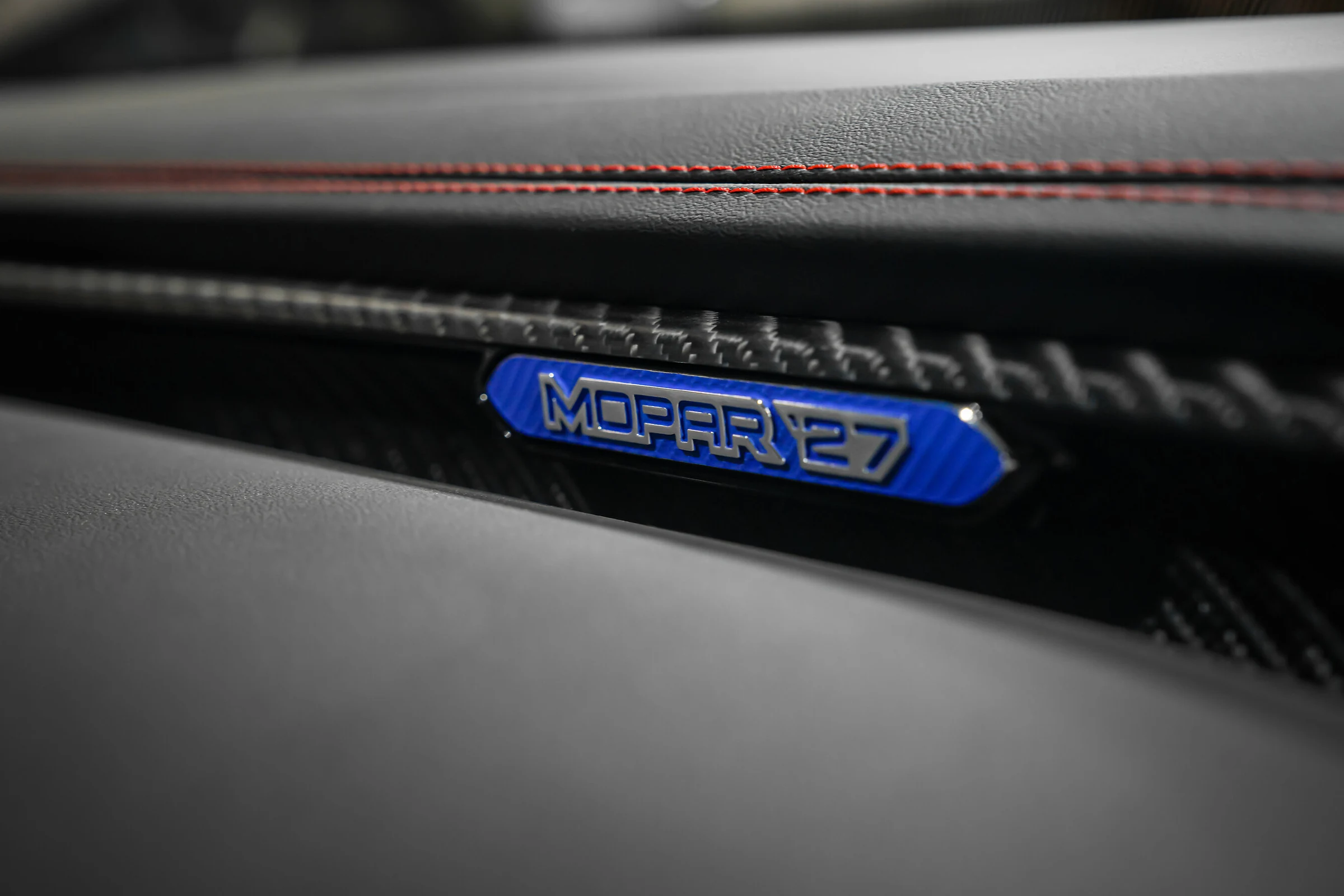 Primer plano de la placa azul «Mopar ’27» sobre el tablero de fibra de carbono de un Dodge Charger