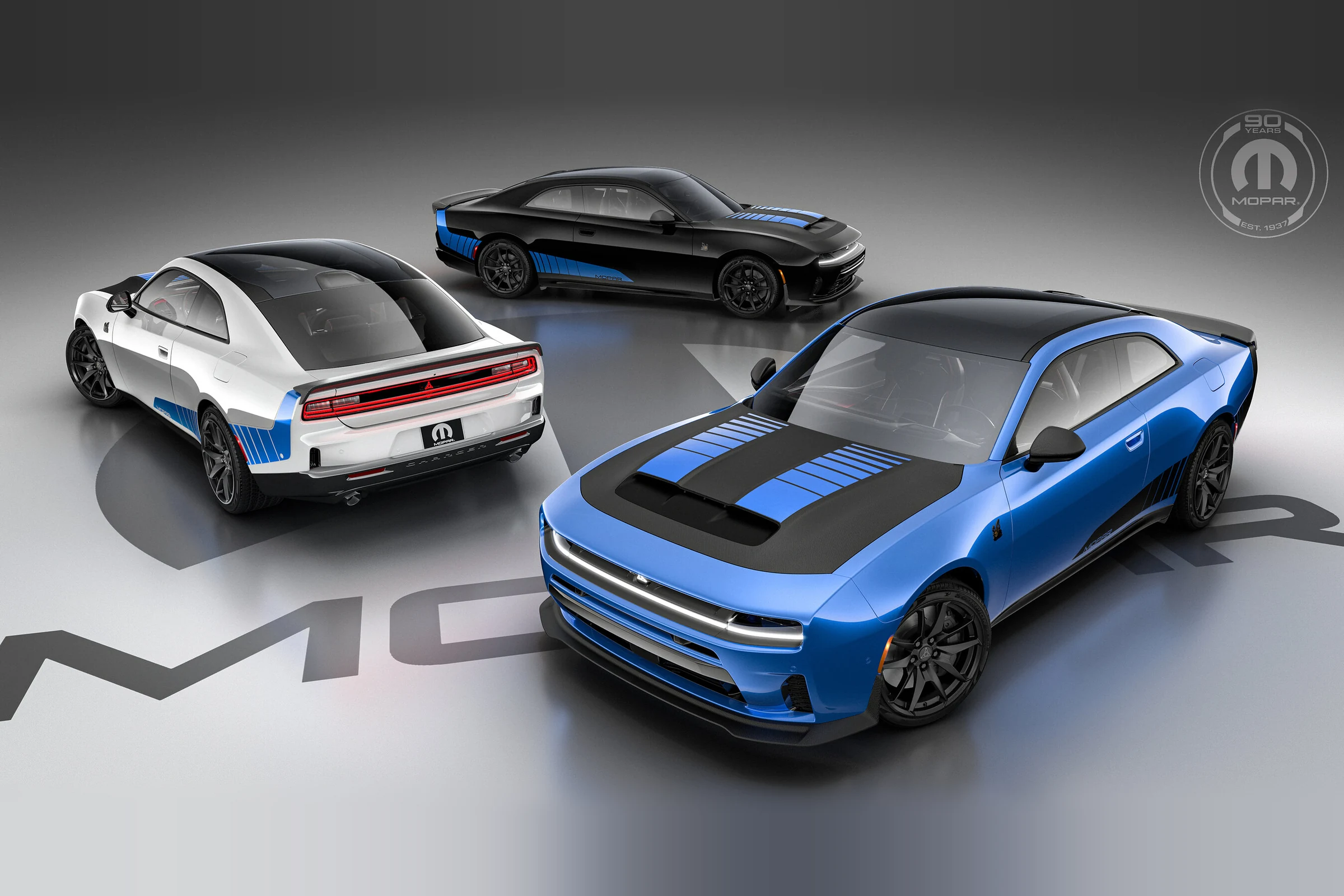 Tres Dodge Charger Mopar ’27 de dos puertas, en azul, negro y blanco, con franjas azules y el logo de los 90 años de Mopar