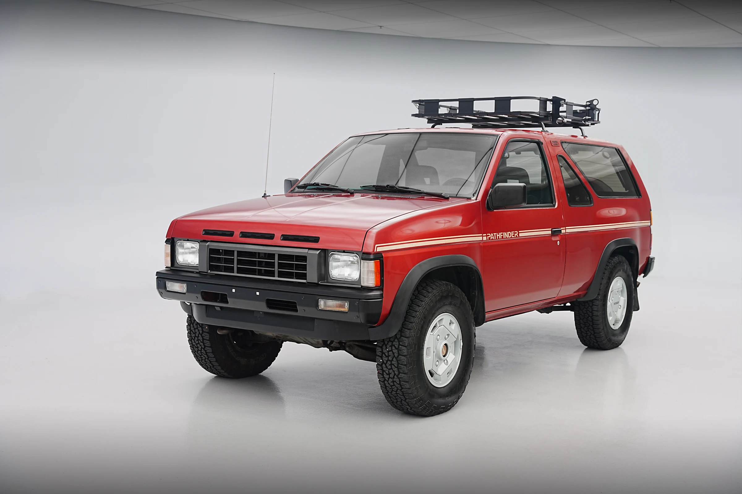 Nissan Pathfinder de 1987, rojo, con portaequipajes en el techo, en un estudio blanco