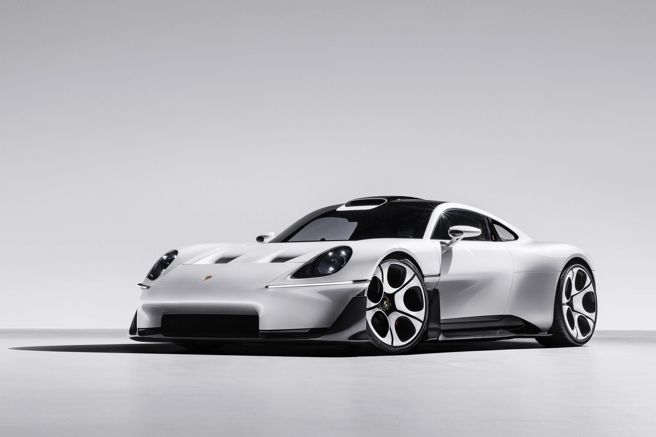Porsche Mission S blanco visto de frente y de costado sobre fondo gris, con faros redondos y llantas de diseño nuevo