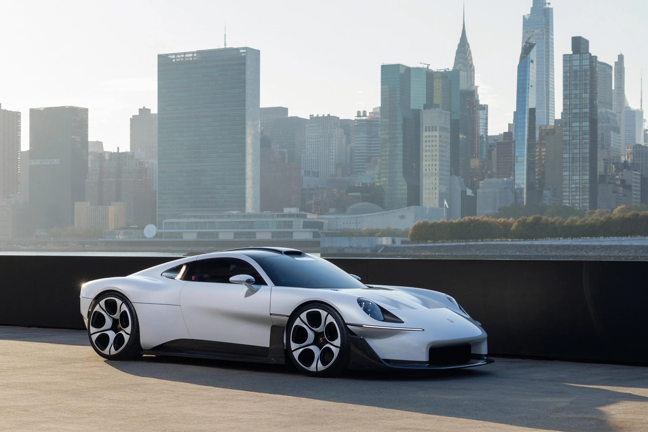 Porsche Mission S blanco estacionado en un muelle de Queens con los edificios de Manhattan al fondo