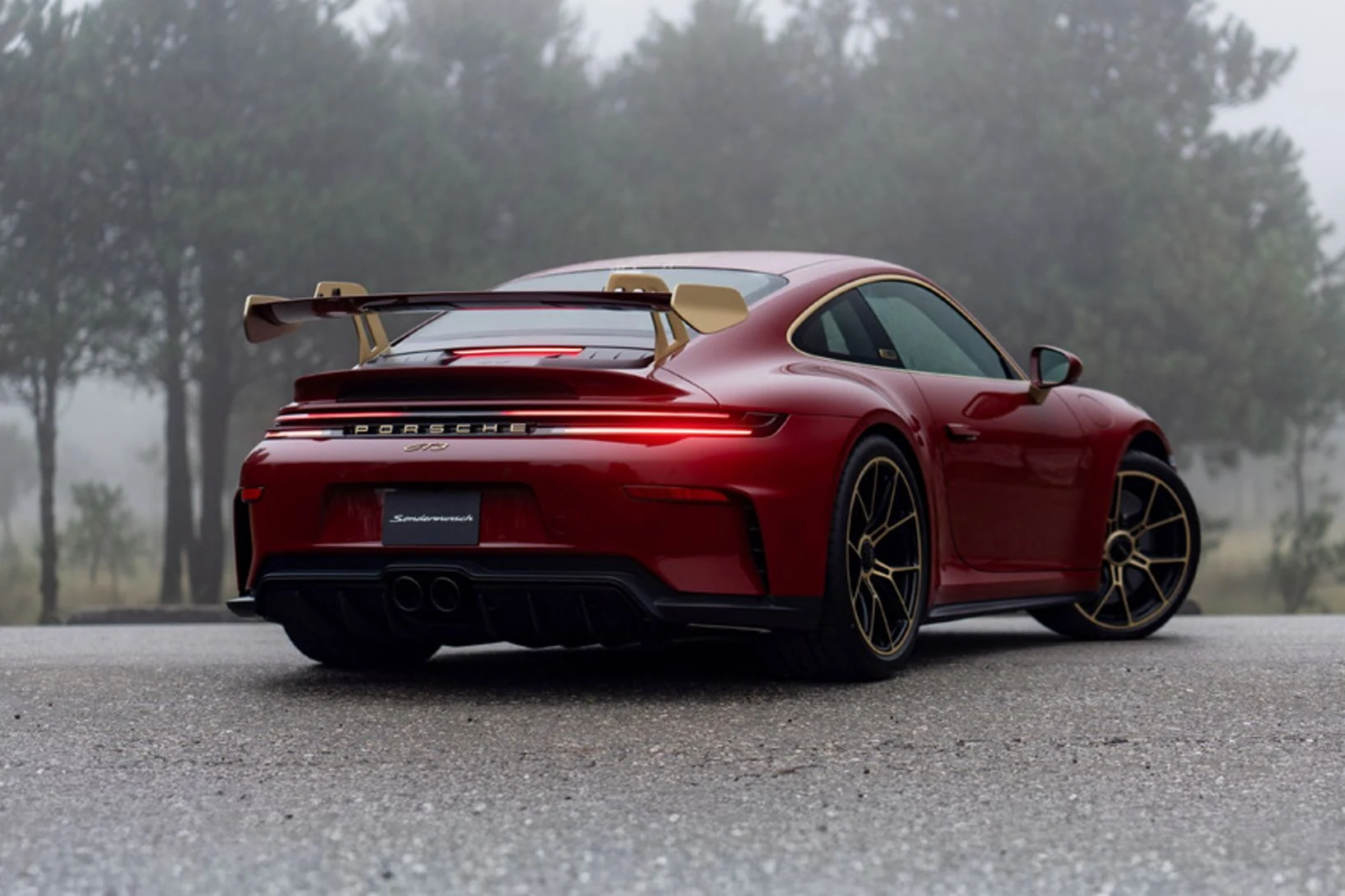 Vista trasera del Porsche 911 GT3 «La Serpiente» rojo sobre un camino de asfalto rodeado de pinos y niebla