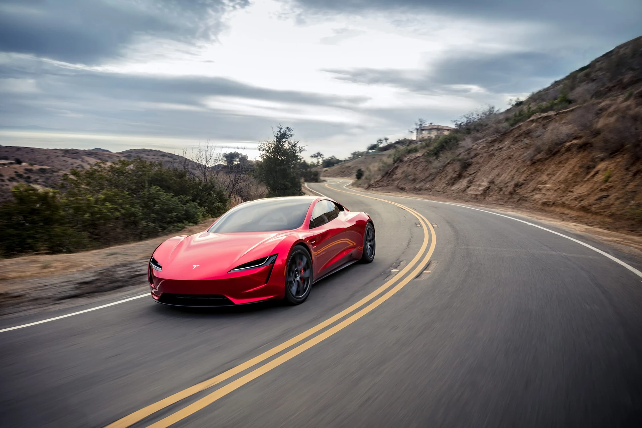 Tesla Roadster rojo, prototipo de 2017, tomando una curva en una carretera con doble línea amarilla