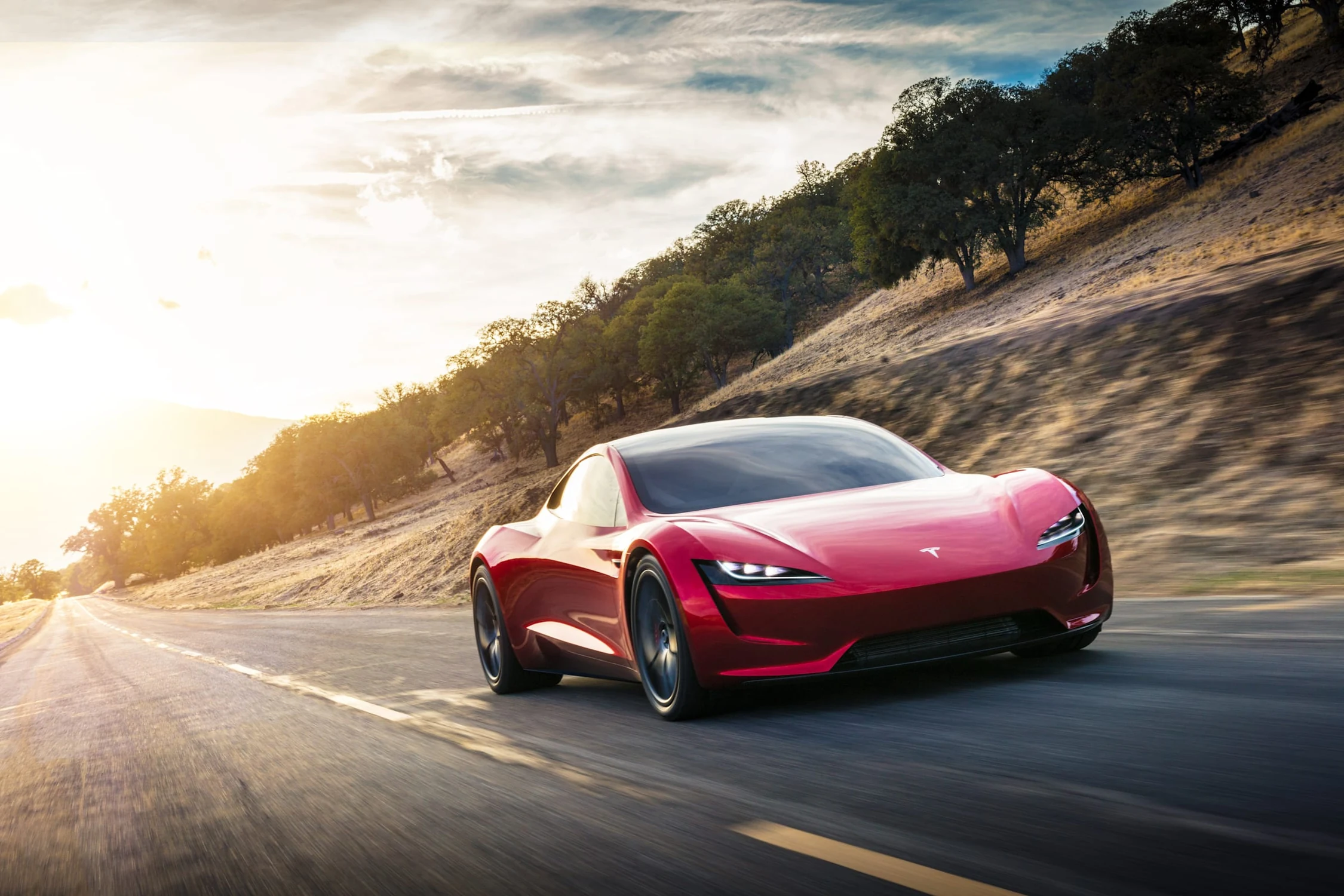 Tesla Roadster rojo, el prototipo de 2017, visto de frente en una carretera de montaña con el sol de fondo