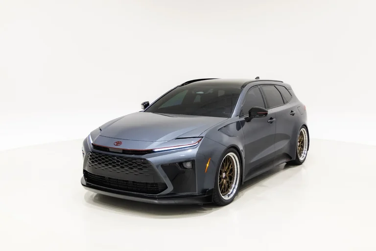 Toyota Crown Signia GT-S Concept gris oscuro visto de tres cuartos frontales, con rines dorados, sobre fondo blanco