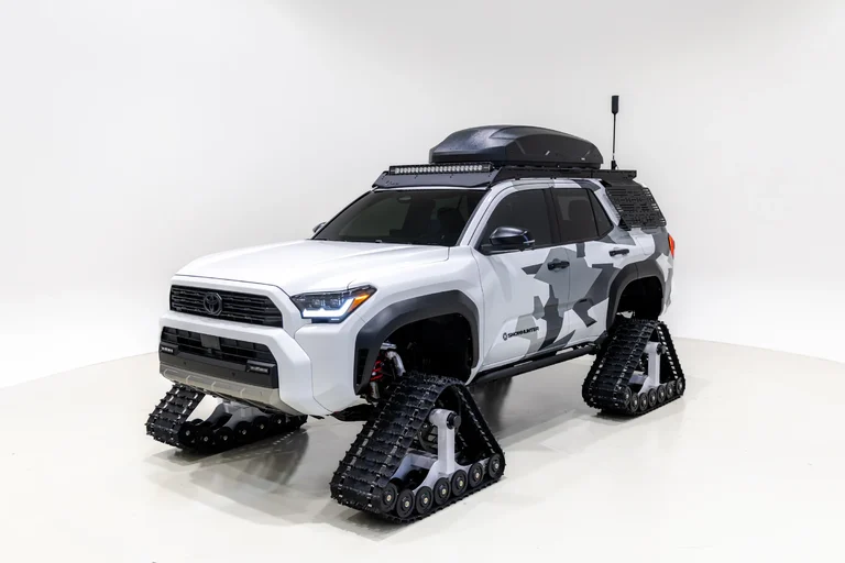 Toyota 4Runner Snowhunter de tres cuartos frontales, con camuflaje gris, detalles negros y orugas, en un estudio blanco