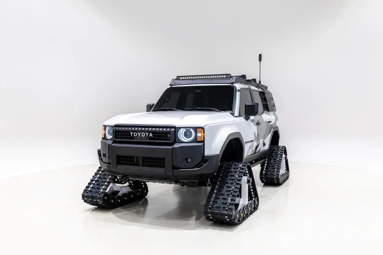 Toyota Land Cruiser Snowhunter blanco con orugas negras y barra de luces, de tres cuartos frontales, en un estudio