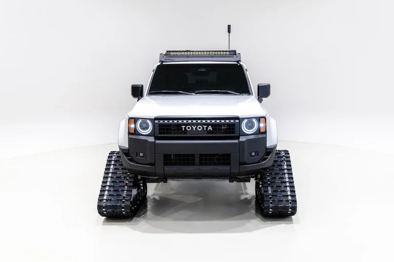 Frente del Land Cruiser Snowhunter blanco, con faros redondos, orugas negras y barra de luces, en un estudio