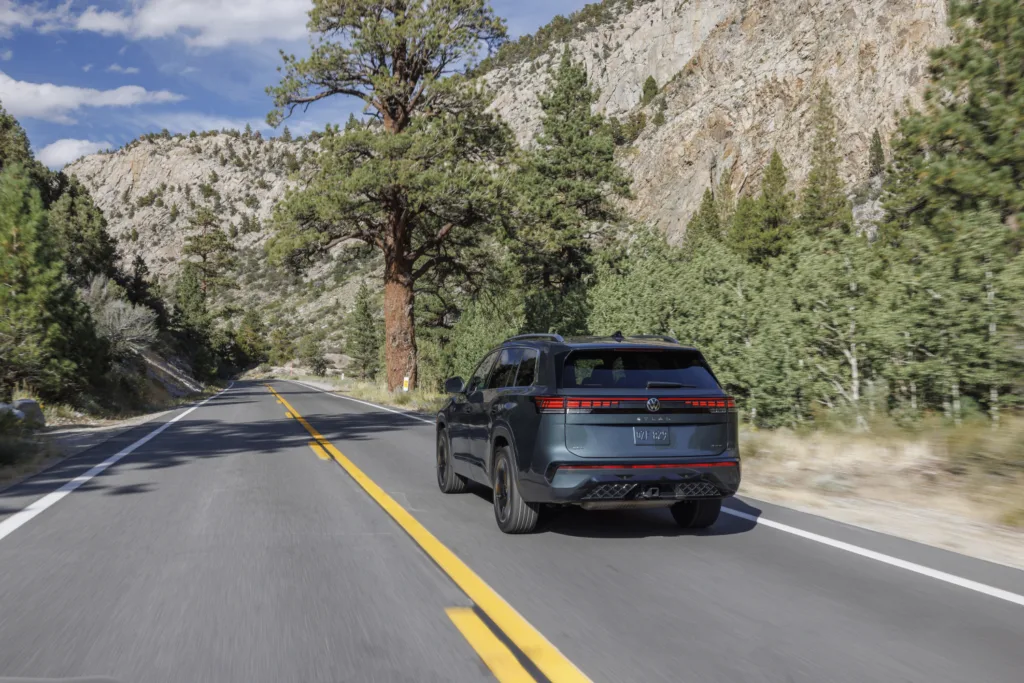 Volkswagen Atlas 2027 por una carretera entre pinos, visto desde atrás