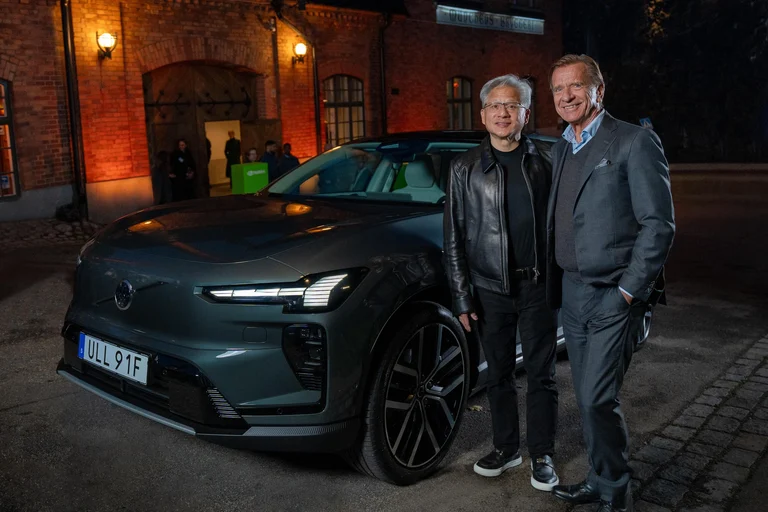 Jensen Huang, de NVIDIA, y Håkan Samuelsson, de Volvo Cars, junto a un Volvo eléctrico gris frente a un edificio de ladrillo