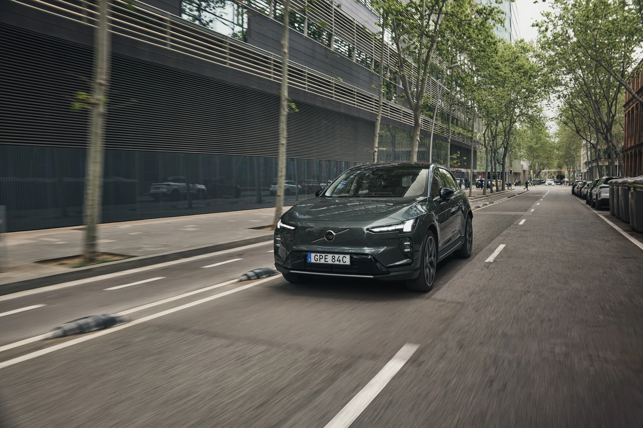 Volvo EX60 de color verde grisáceo circula por una calle arbolada de una ciudad europea