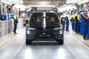 Un Volvo EX60 negro avanza por la línea de montaje de Volvo, con operarios de ropa amarilla y azul a los lados