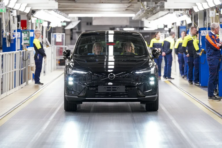 Un Volvo EX60 negro avanza por la línea de montaje de Volvo, con operarios de ropa amarilla y azul a los lados
