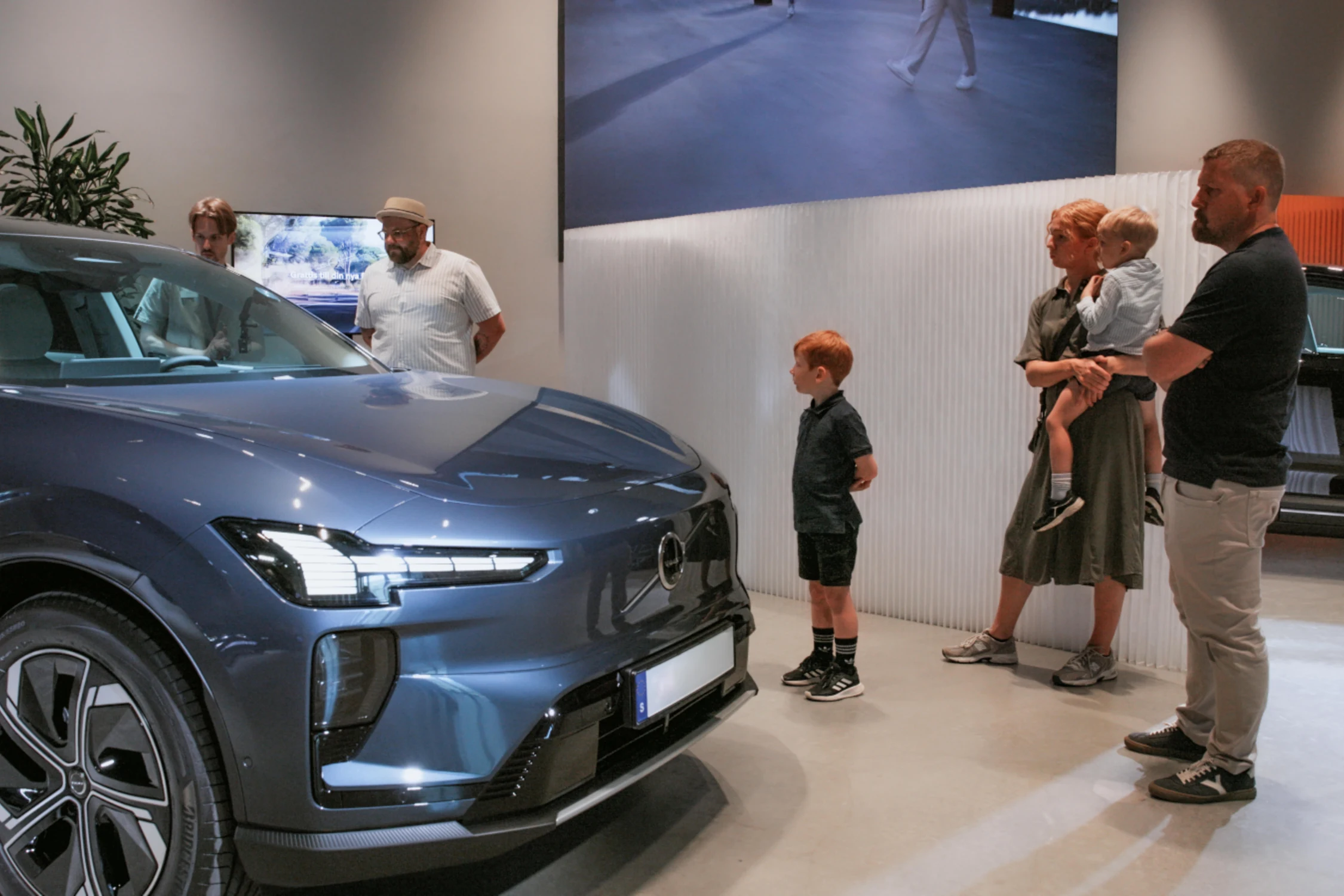 Una familia observa un Volvo EX60 azul en una sala de exhibición durante las primeras entregas a clientes